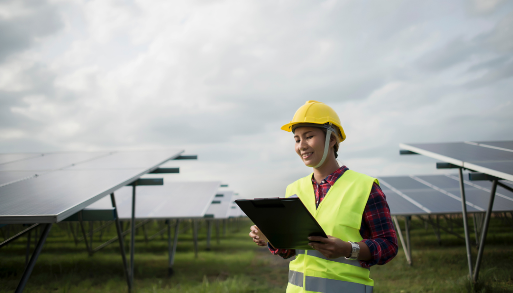A photo of a woman reviewing a clipboard in front of a solar farm